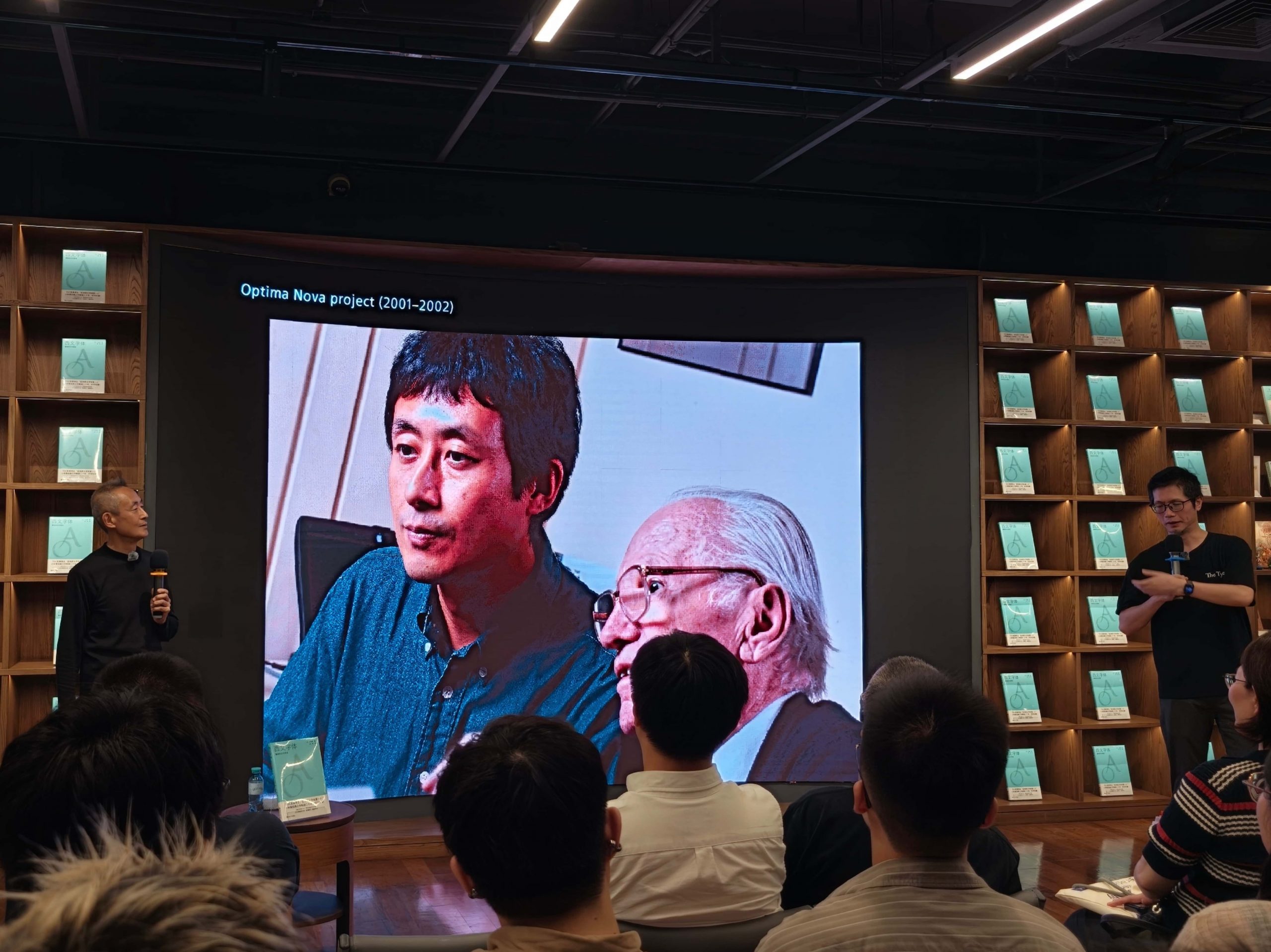 小林章与刘庆分立投影幕两侧,观众观看屏幕上小林章与察普夫 2001 至 2002 年一起共事 Optima Nova project 的工作合影。